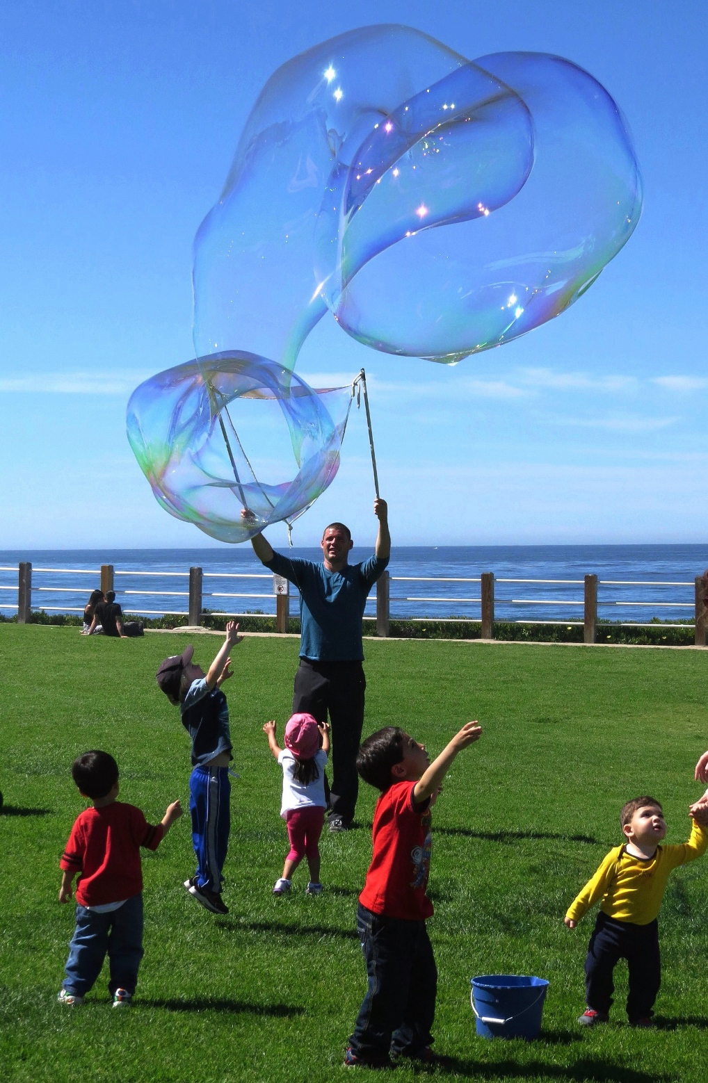A person creating large bubbles above children playing with them